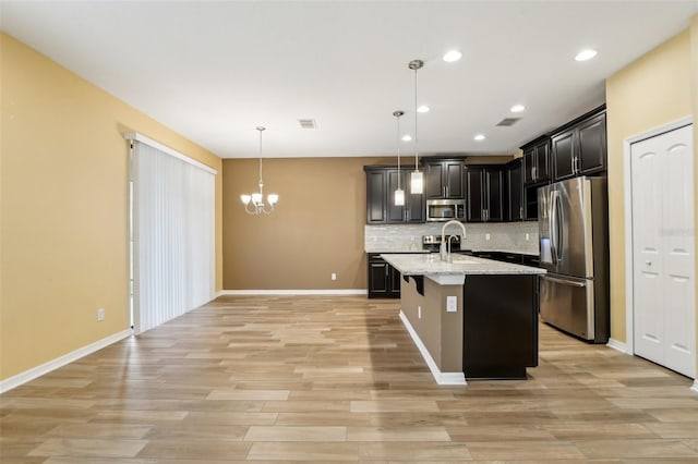 kitchen featuring pendant lighting, a kitchen island with sink, light wood-type flooring, light stone countertops, and stainless steel appliances