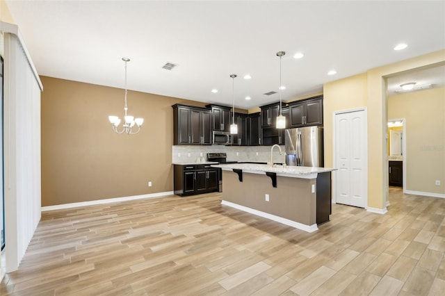 kitchen with a kitchen bar, an island with sink, hanging light fixtures, and appliances with stainless steel finishes