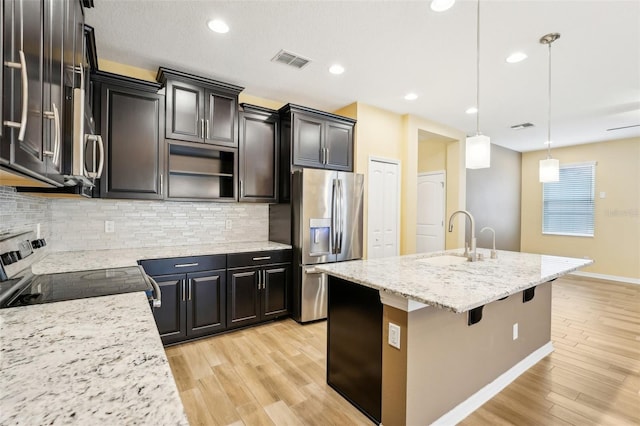 kitchen featuring pendant lighting, a kitchen island with sink, sink, range with electric cooktop, and stainless steel refrigerator with ice dispenser