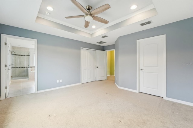 unfurnished bedroom featuring ceiling fan, a raised ceiling, ensuite bathroom, light colored carpet, and a closet