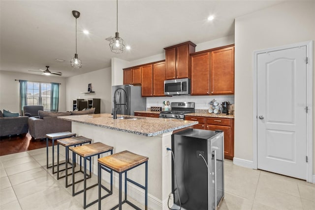 kitchen featuring a kitchen bar, stainless steel appliances, ceiling fan, sink, and an island with sink