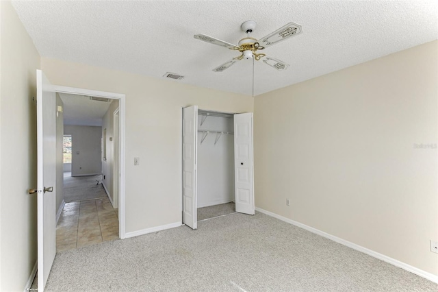 unfurnished bedroom featuring ceiling fan, a closet, light colored carpet, and a textured ceiling