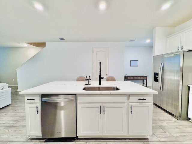 kitchen featuring light stone countertops, appliances with stainless steel finishes, a kitchen island with sink, sink, and white cabinetry