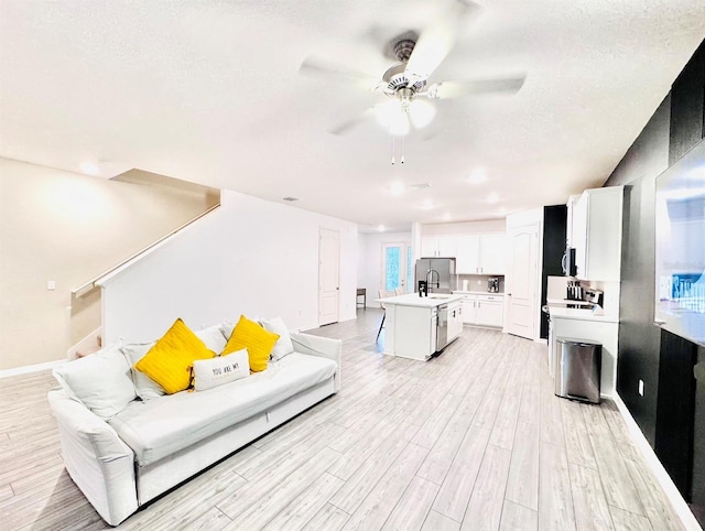 living room with ceiling fan, sink, light wood-type flooring, and a textured ceiling