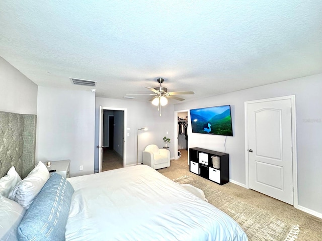 carpeted bedroom featuring a walk in closet, ceiling fan, a closet, and a textured ceiling