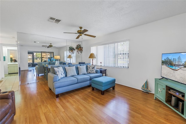 living room featuring ceiling fan, a textured ceiling, and light wood-type flooring