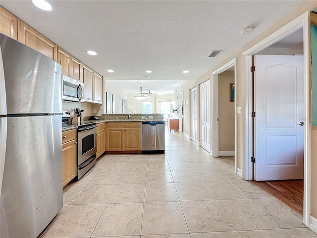 kitchen with sink, stainless steel appliances, kitchen peninsula, light brown cabinetry, and light tile patterned flooring