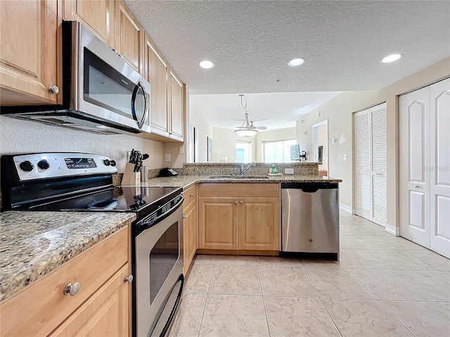 kitchen featuring sink, stainless steel appliances, light stone counters, pendant lighting, and a textured ceiling