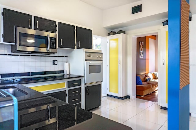 kitchen with stainless steel microwave, visible vents, oven, stovetop, and dark cabinetry