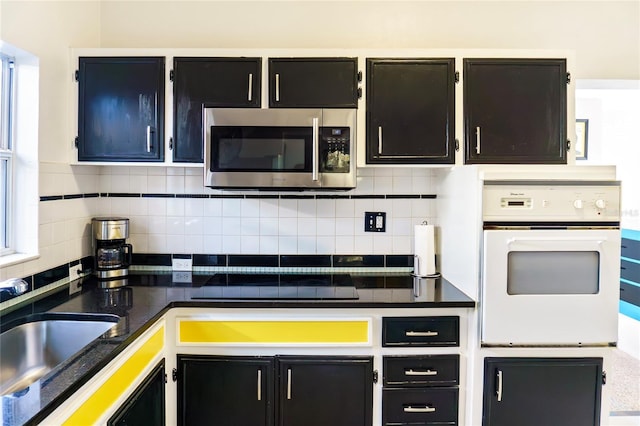 kitchen featuring stainless steel microwave, dark countertops, backsplash, and oven