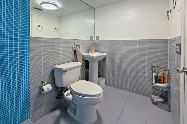 bathroom featuring visible vents, toilet, tile patterned floors, tile walls, and a sink