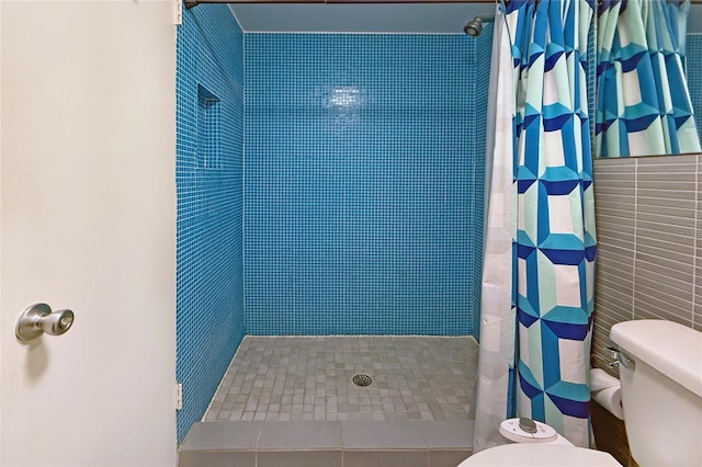 bathroom with toilet, tiled shower, and tile walls