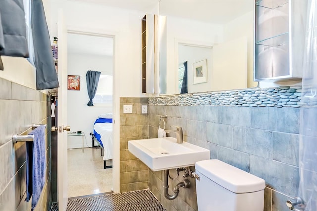 half bath featuring ensuite bath, toilet, tile walls, and a sink