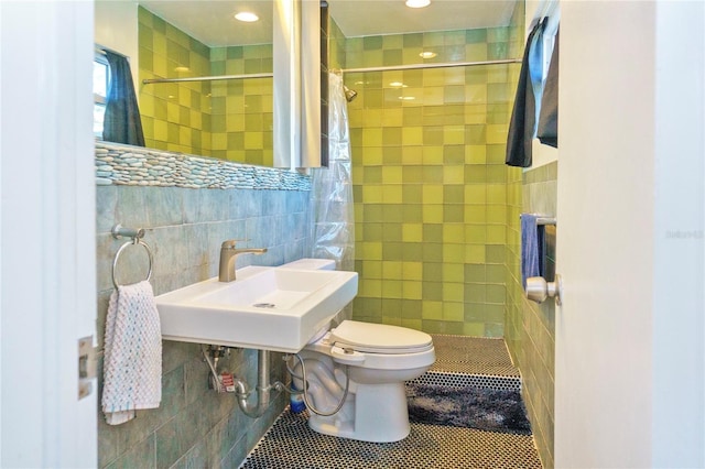 bathroom featuring a sink, toilet, tile walls, and a tile shower