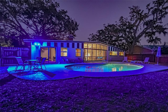 pool at night featuring a fenced in pool, a patio area, and fence