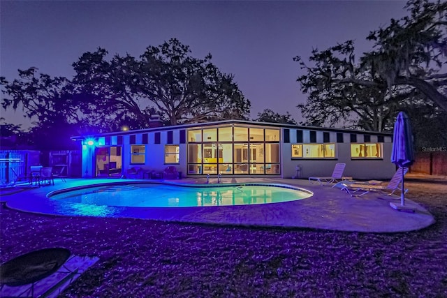 pool at night with a patio, fence, and an outdoor pool