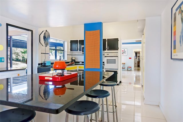 kitchen featuring light tile patterned floors, tasteful backsplash, dark countertops, and a breakfast bar area