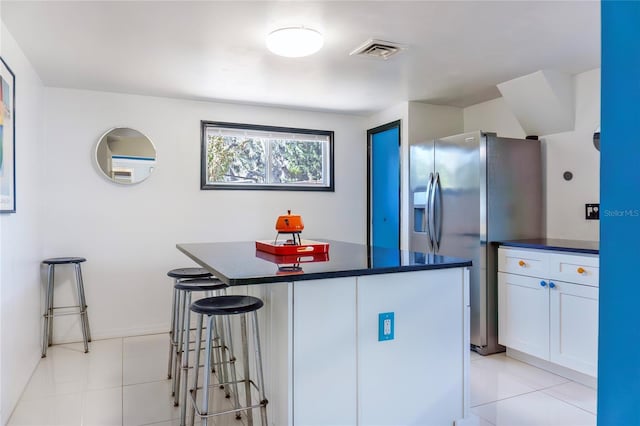 kitchen with visible vents, dark countertops, a kitchen breakfast bar, stainless steel fridge, and a center island