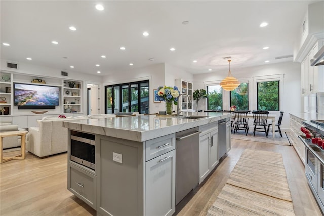 kitchen featuring light stone countertops, sink, hanging light fixtures, stainless steel appliances, and a large island with sink