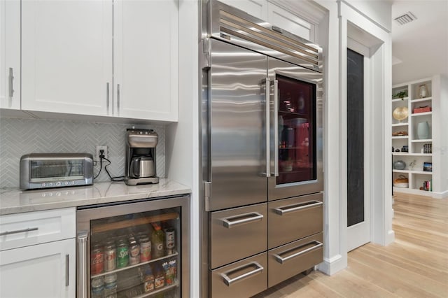 kitchen featuring light stone countertops, wine cooler, built in refrigerator, decorative backsplash, and white cabinets