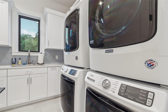 clothes washing area featuring cabinets, sink, light tile patterned floors, and stacked washing maching and dryer