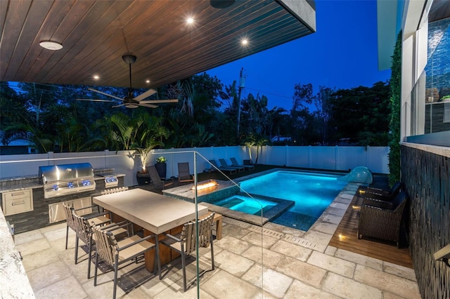 pool at night featuring an in ground hot tub, ceiling fan, grilling area, a patio, and an outdoor bar