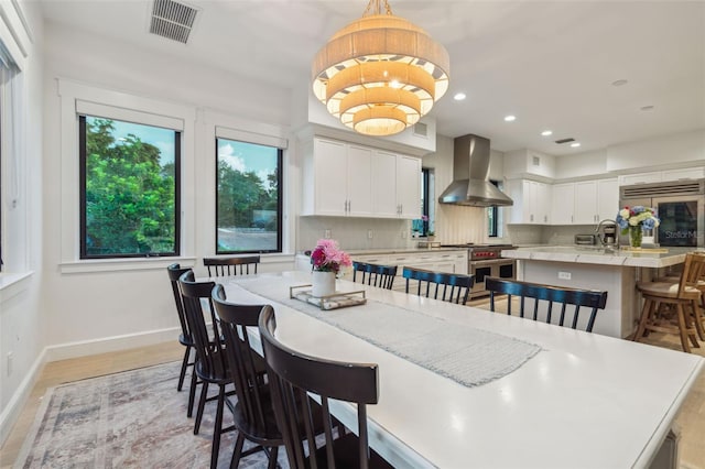 kitchen featuring wall chimney exhaust hood, a breakfast bar, high end appliances, white cabinetry, and hanging light fixtures