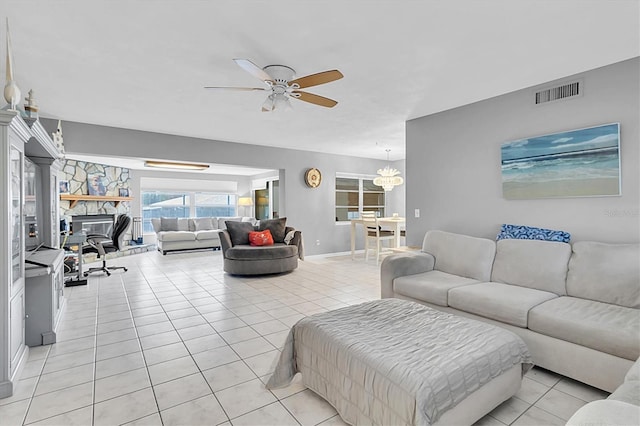 tiled living room featuring ceiling fan with notable chandelier and a stone fireplace