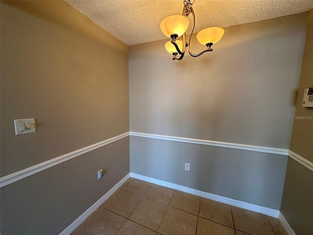 unfurnished dining area featuring tile patterned flooring, a textured ceiling, and an inviting chandelier