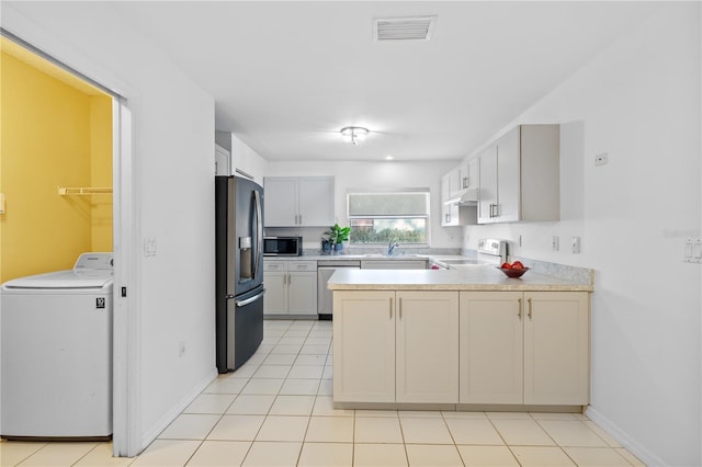 kitchen with washer / dryer, sink, light tile patterned floors, appliances with stainless steel finishes, and white cabinets