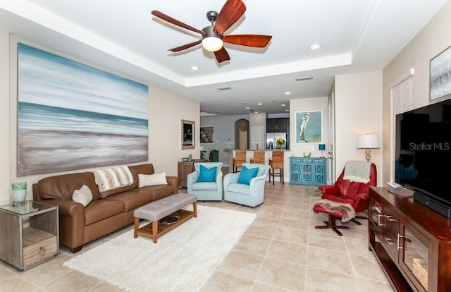 living room featuring a tray ceiling, ceiling fan, and light tile patterned floors