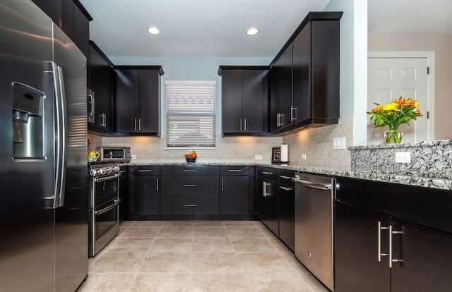 kitchen featuring backsplash, light stone counters, light tile patterned flooring, and stainless steel appliances