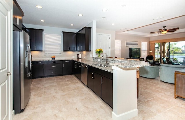 kitchen featuring sink, ceiling fan, light stone countertops, appliances with stainless steel finishes, and kitchen peninsula