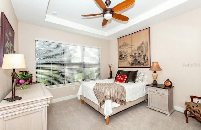 bedroom featuring ceiling fan, a raised ceiling, and light colored carpet