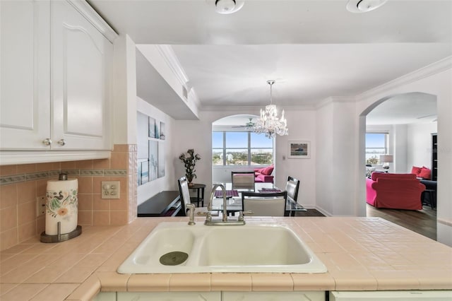 kitchen featuring a notable chandelier, crown molding, sink, white cabinets, and tile countertops