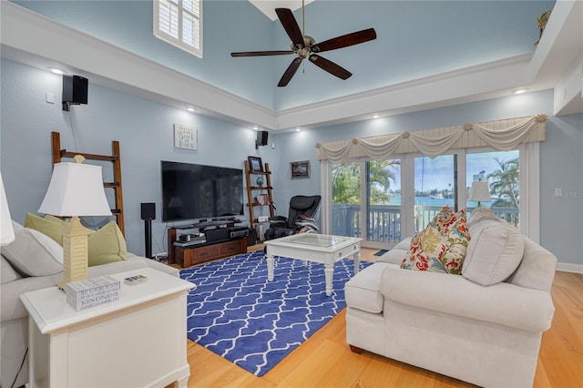 living room with hardwood / wood-style flooring, ceiling fan, and a towering ceiling