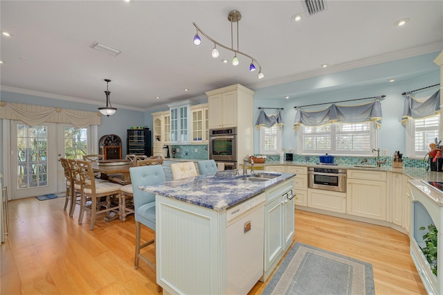 kitchen featuring double oven, crown molding, sink, decorative light fixtures, and an island with sink