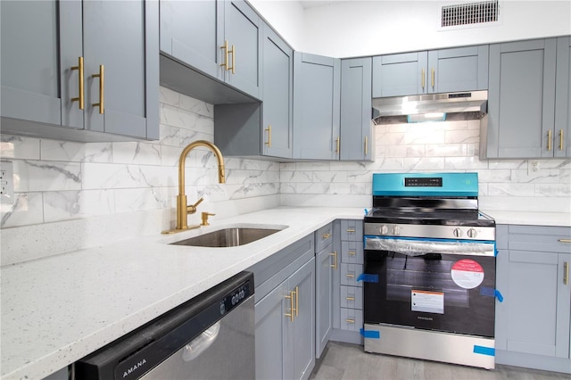 kitchen with sink, backsplash, gray cabinetry, light stone countertops, and stainless steel appliances