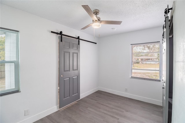 unfurnished bedroom featuring ceiling fan, wood-type flooring, and a barn door