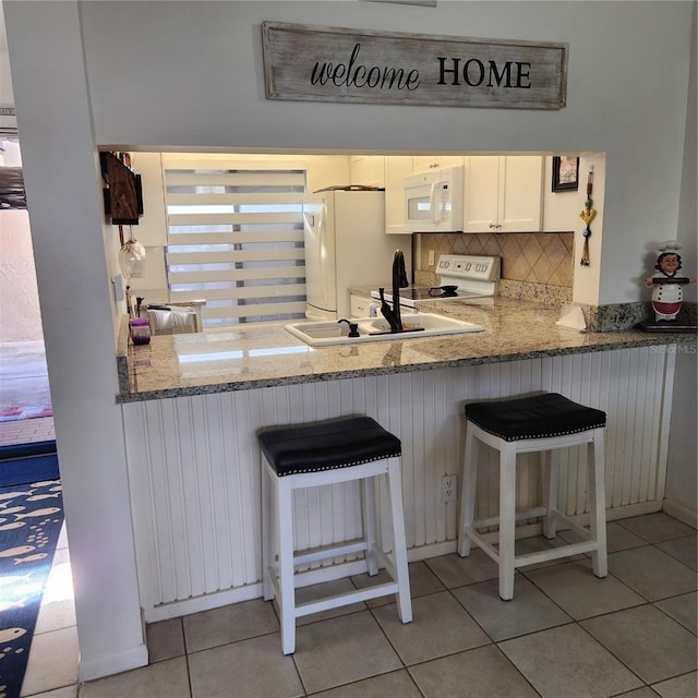 kitchen featuring white cabinets, a kitchen breakfast bar, decorative backsplash, and white appliances