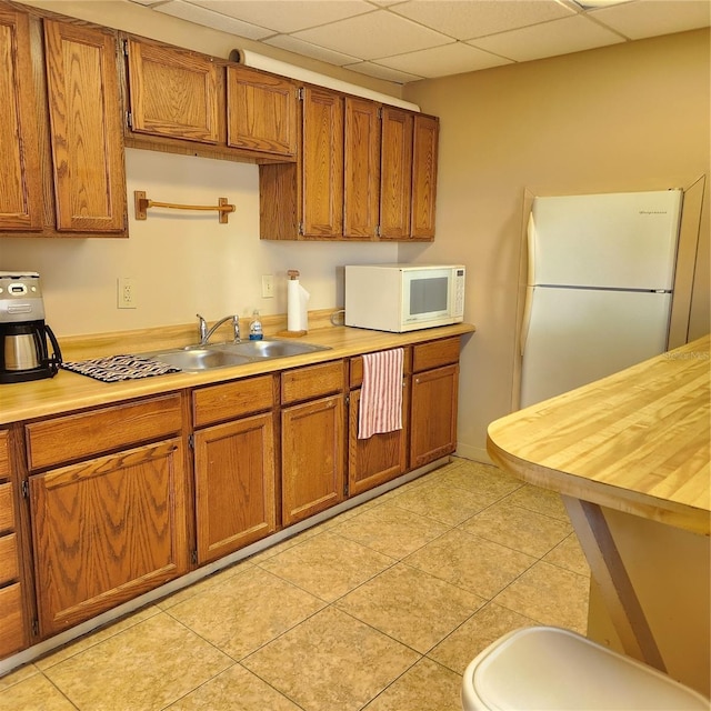 kitchen featuring a drop ceiling, light tile patterned floors, white appliances, and sink