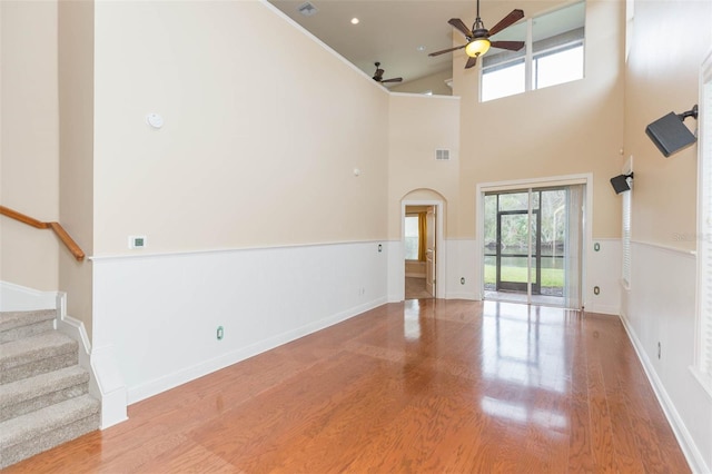 unfurnished living room with ceiling fan, light hardwood / wood-style floors, and a high ceiling