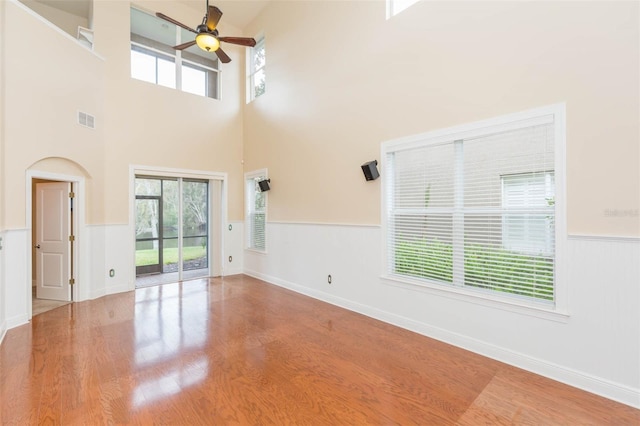 interior space with ceiling fan, a towering ceiling, a healthy amount of sunlight, and wood-type flooring