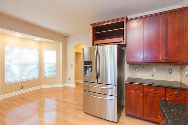 kitchen with decorative backsplash, light hardwood / wood-style flooring, dark stone counters, and stainless steel refrigerator with ice dispenser