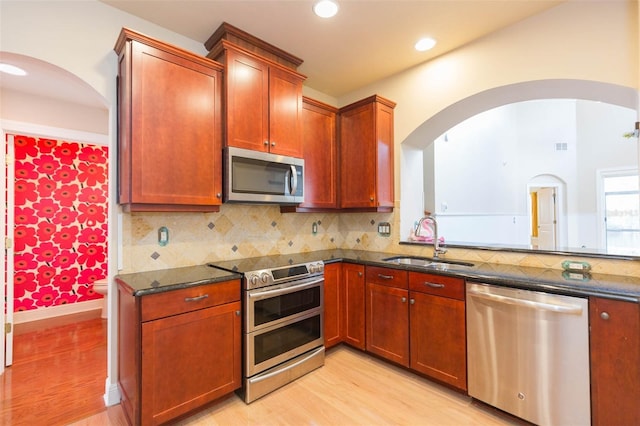 kitchen featuring backsplash, sink, dark stone countertops, light hardwood / wood-style floors, and stainless steel appliances