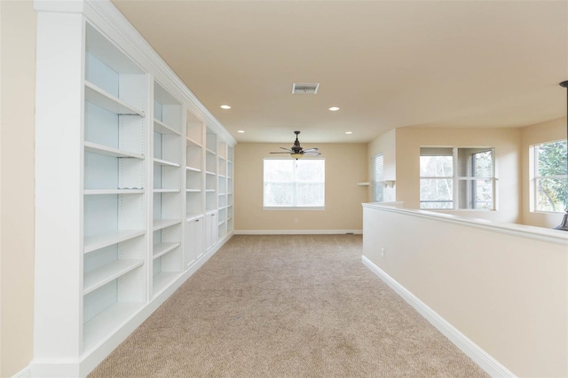 spare room with ceiling fan, light colored carpet, built in features, and a wealth of natural light