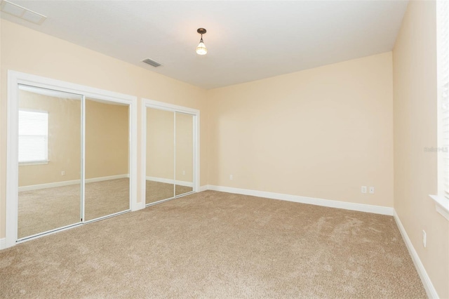 unfurnished bedroom featuring carpet flooring and multiple closets