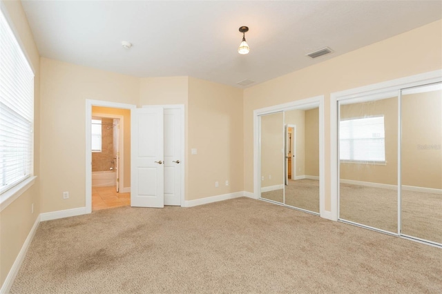 unfurnished bedroom with ensuite bath, light carpet, and multiple windows