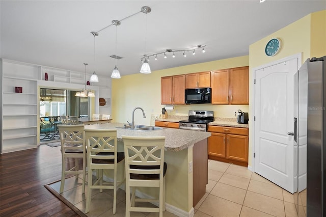 kitchen with sink, stainless steel appliances, an island with sink, pendant lighting, and a kitchen bar