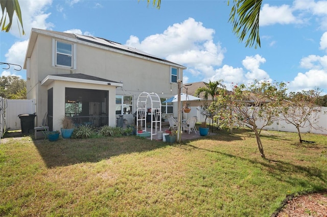 rear view of property featuring solar panels, a sunroom, and a lawn